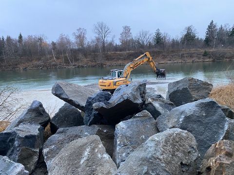 Wasserbausteine am Ufer, im Hintergrund der Bagger auf der Kiesbank im Lech